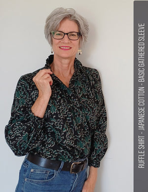 Middle aged woman stands holding the front edge of her frill neck collared blouse she has sewn from Japanese cotton.